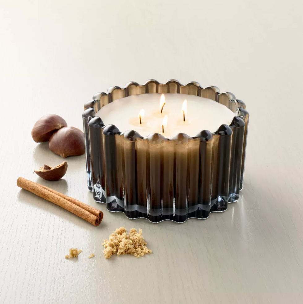 Lit candle in a fluted glass holder with cinnamon, nuts, and brown sugar.
