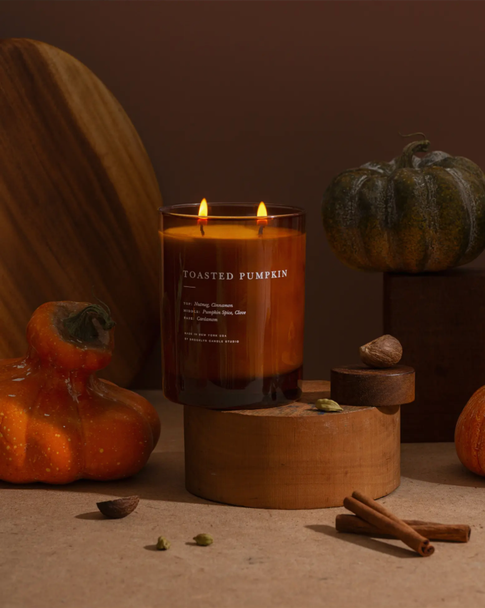 Lit "Toasted Pumpkin" candle with pumpkins, spices, and warm autumn decor.