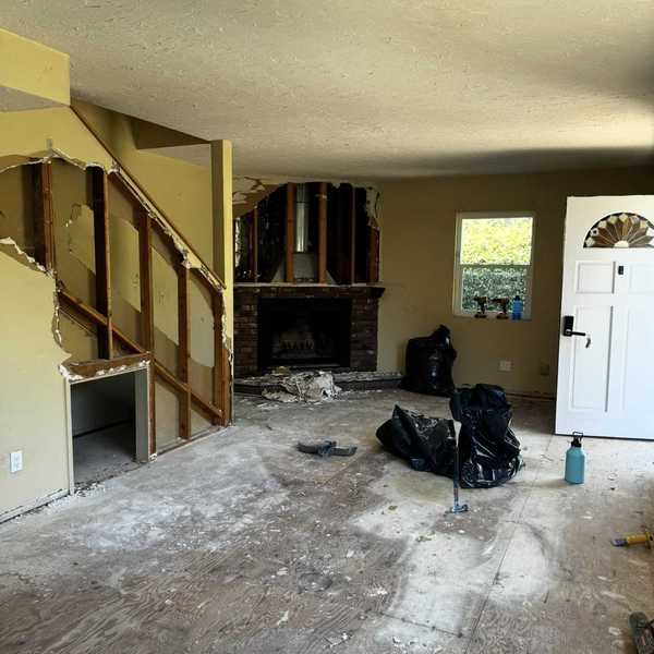 Living room under renovation, with exposed walls and debris on the floor.