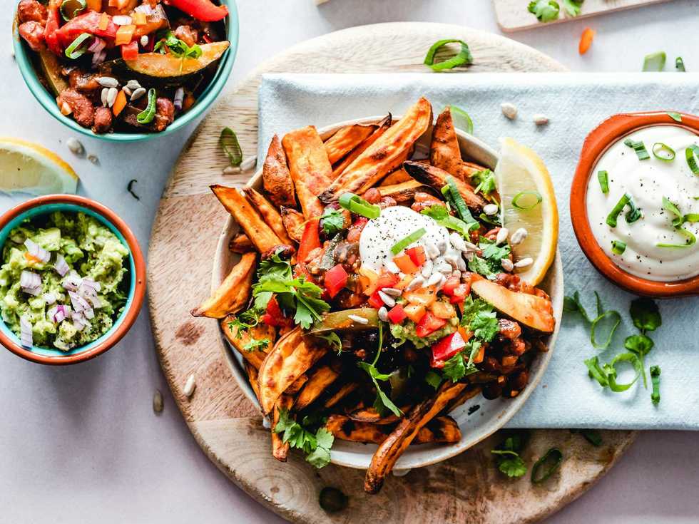 Loaded sweet potato fries with toppings, served with dips and garnished with herbs.