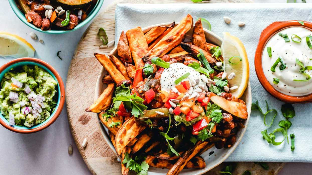 Loaded sweet potato fries with toppings, served with dips and garnished with herbs.
