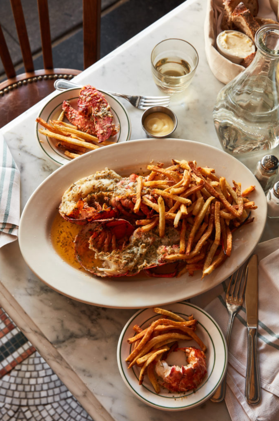 Lobster with fries on a marble table, wine, and breadbasket.