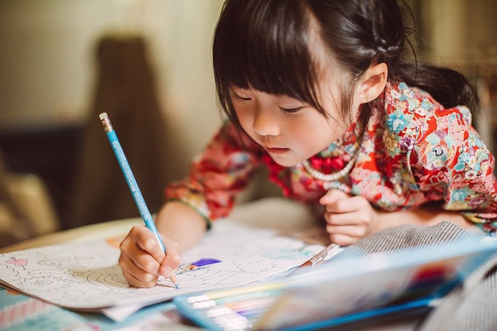 Lovely little girl in traditional Chinese costumes concentrate on colouring a colouring book happily.
