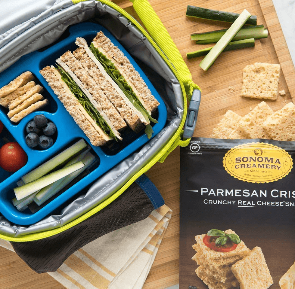 Lunchbox with sandwich, veggies, berries, crackers; Parmesan Crisps on cutting board.