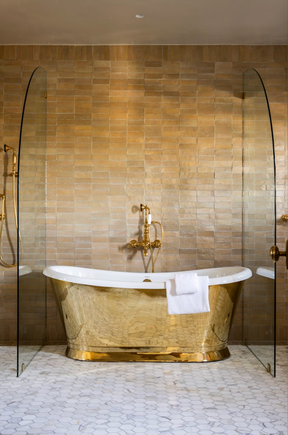 Luxurious bathroom with gold bathtub, tiled wall, and hexagonal floor tiles.