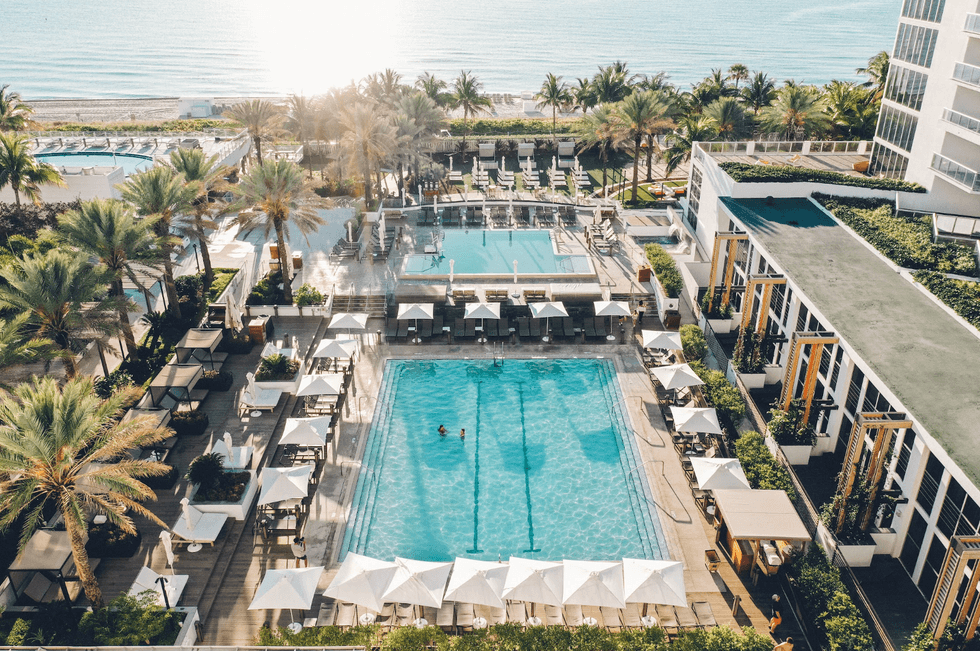 Luxurious beachfront resort with palm trees and two pools overlooking the ocean.