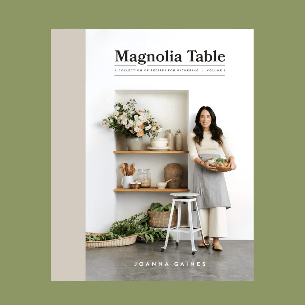 "Magnolia Table Volume 2 cookbook cover with a woman holding a bowl beside kitchen shelves."