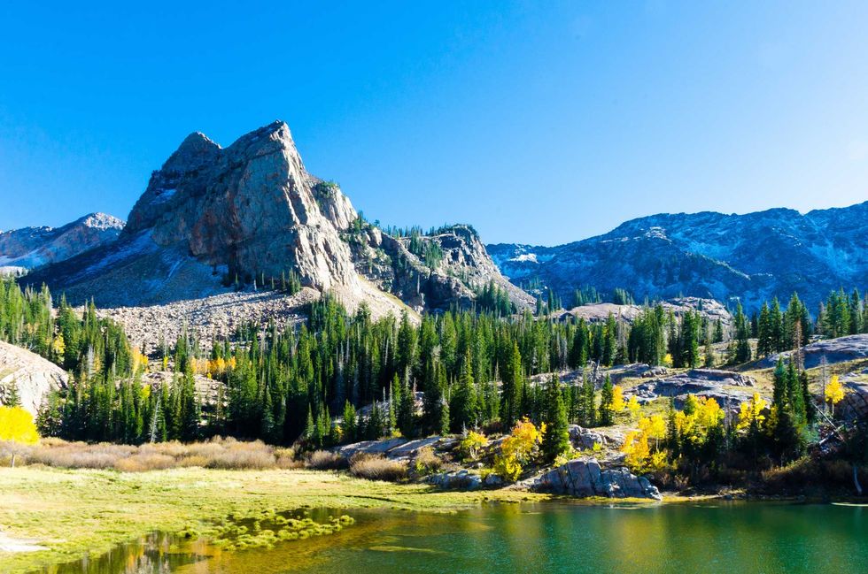 Majestic mountain landscape with pine trees, clear blue sky, and a calm lake in the foreground.