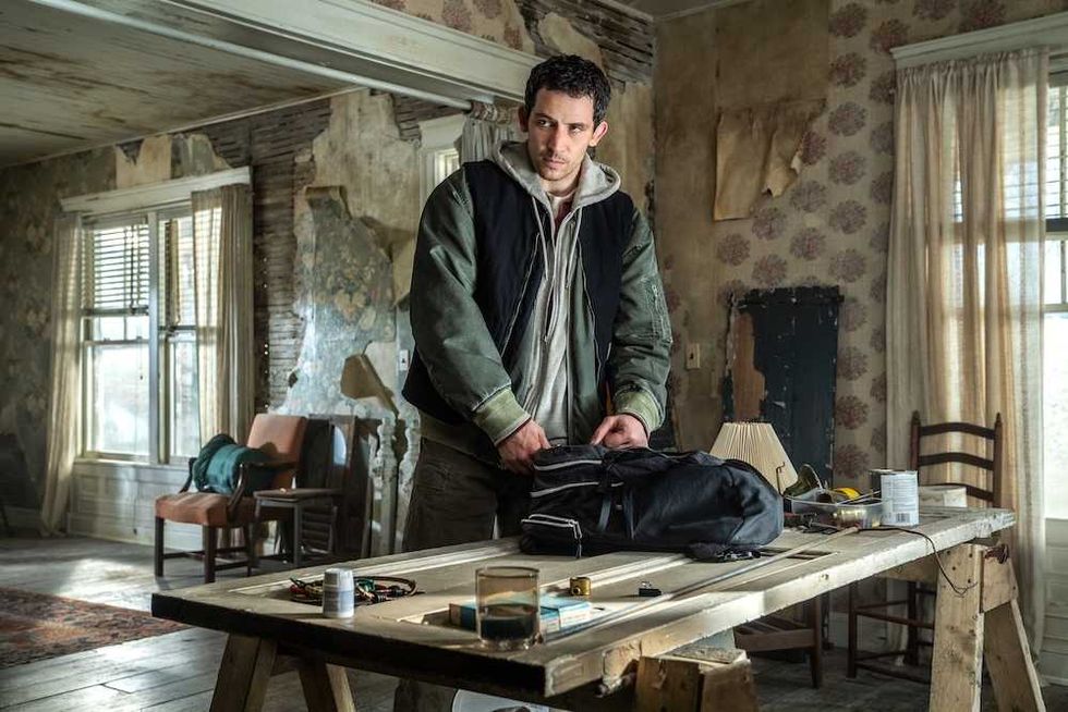 Man in a dilapidated room packing a bag on a wooden table.