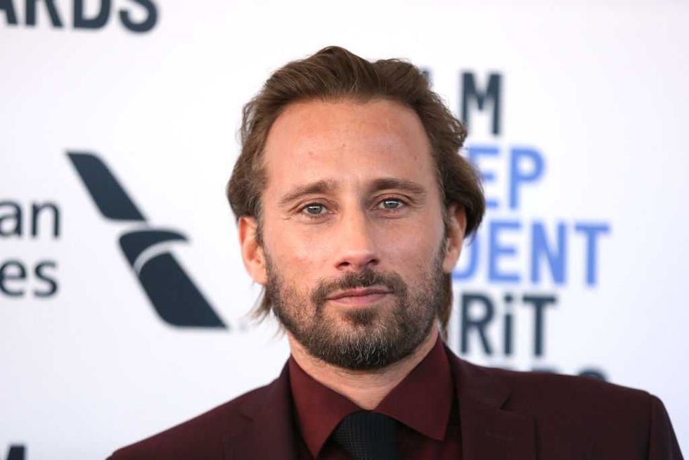 Man in a maroon suit at an event, backdrop with blue and black text.