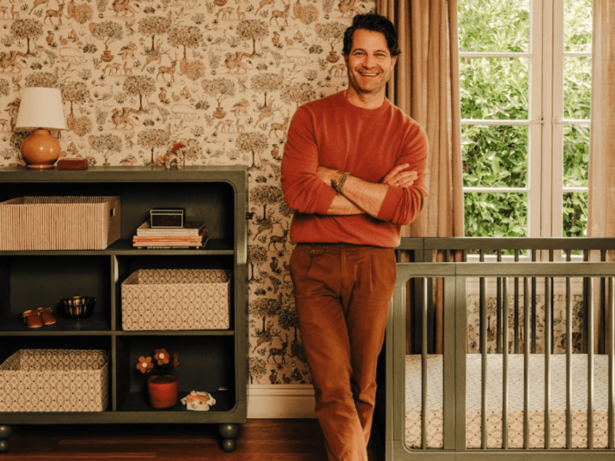 Man in a stylish nursery with animal wallpaper, next to crib and shelf.