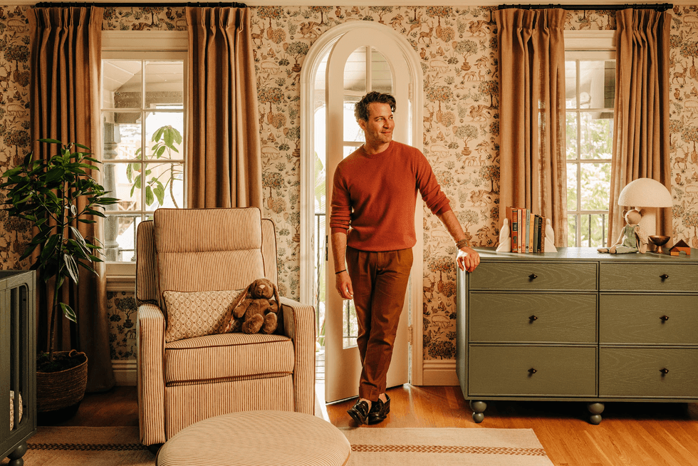 Man in cozy living room with floral wallpaper and earthy tones.