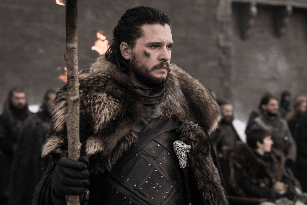 Man in fur cloak and armor holds torch, standing serious among others in medieval setting.