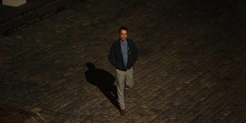 Man walking alone on a dimly lit cobblestone street at night.