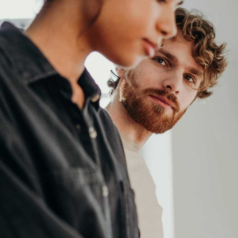 Man with a beard looks at a woman in focus, indoors.