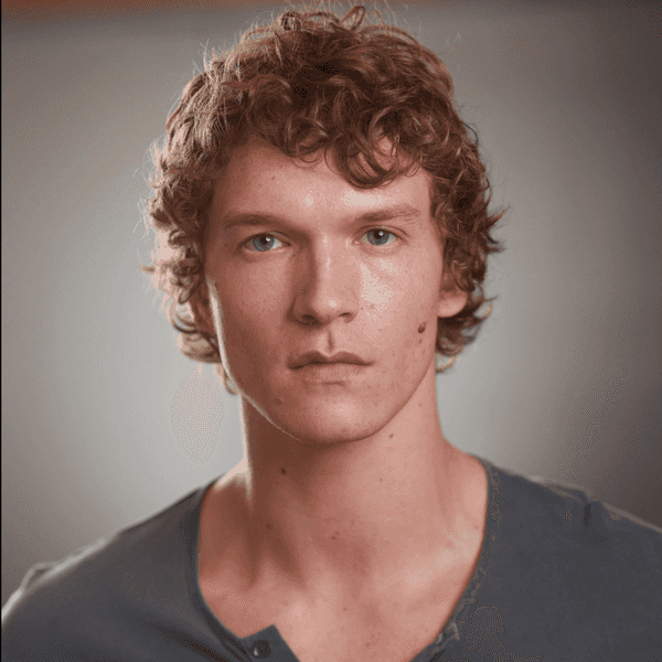 Man with curly hair in a blue shirt against a neutral background.