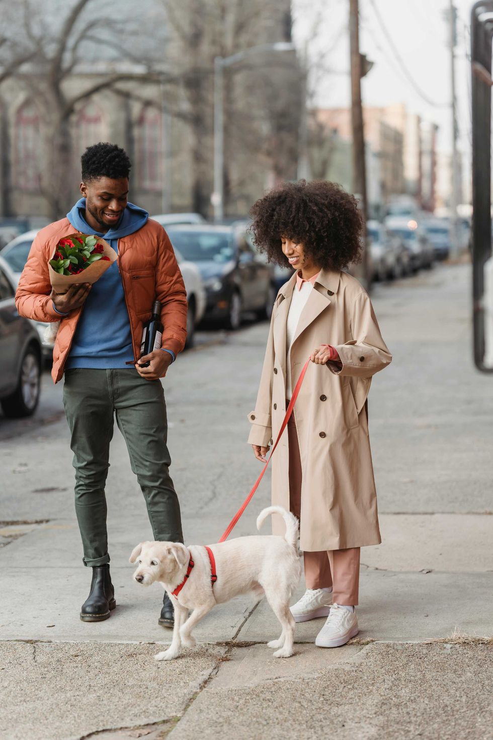 Man with flowers and woman walking a dog on a city sidewalk.