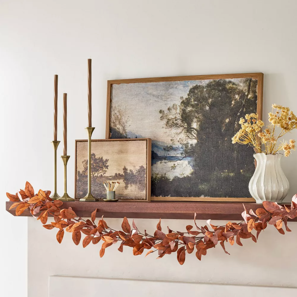 Mantel with landscape paintings, candlesticks, vase, and autumn leaf garland.