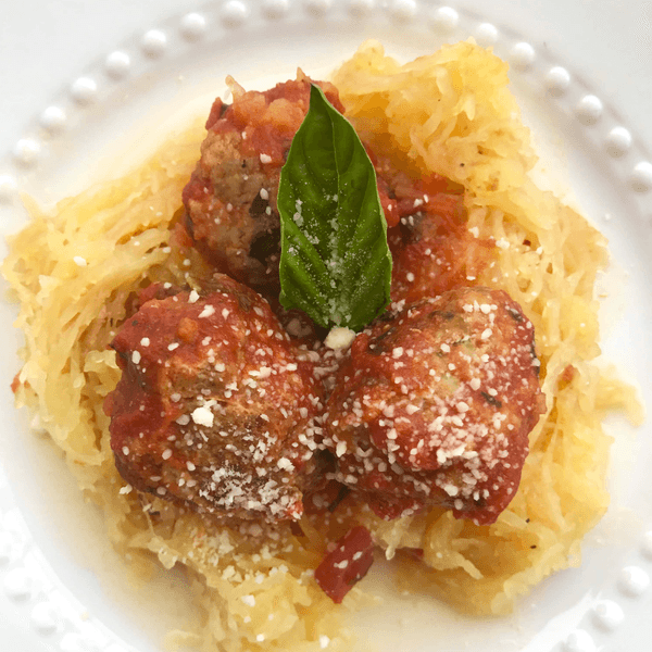 Meatballs with marinara on spaghetti squash, garnished with fresh basil and grated cheese.