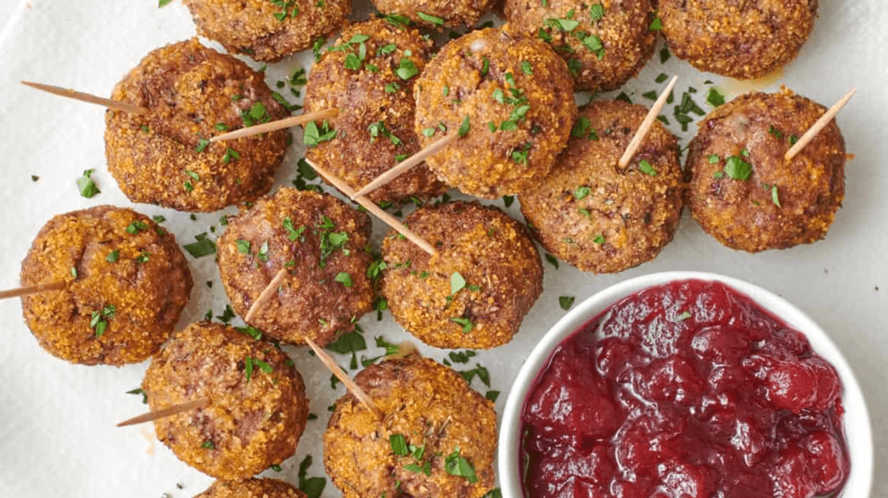 Meatballs with parsley garnish and toothpicks, served with cranberry sauce on a white plate.