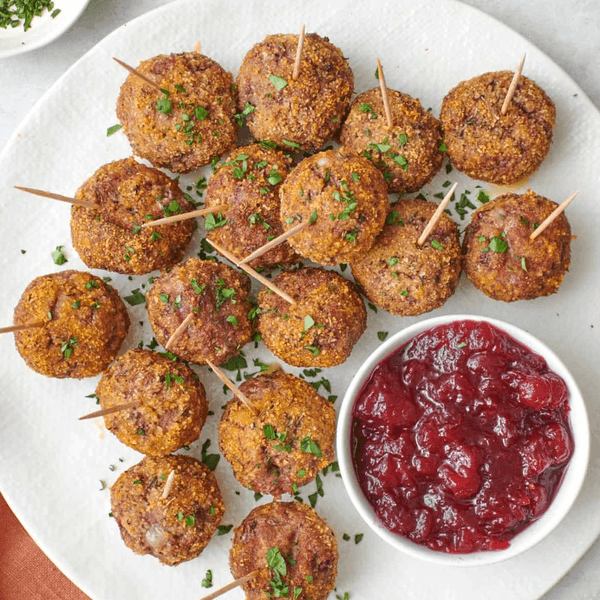 Meatballs with parsley garnish and toothpicks, served with cranberry sauce on a white plate.