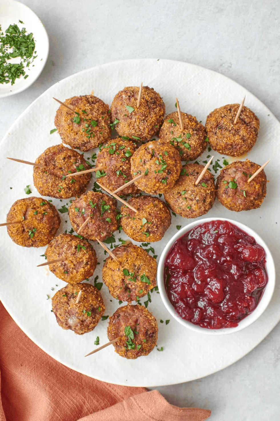Meatballs with parsley garnish and toothpicks, served with cranberry sauce on a white plate.