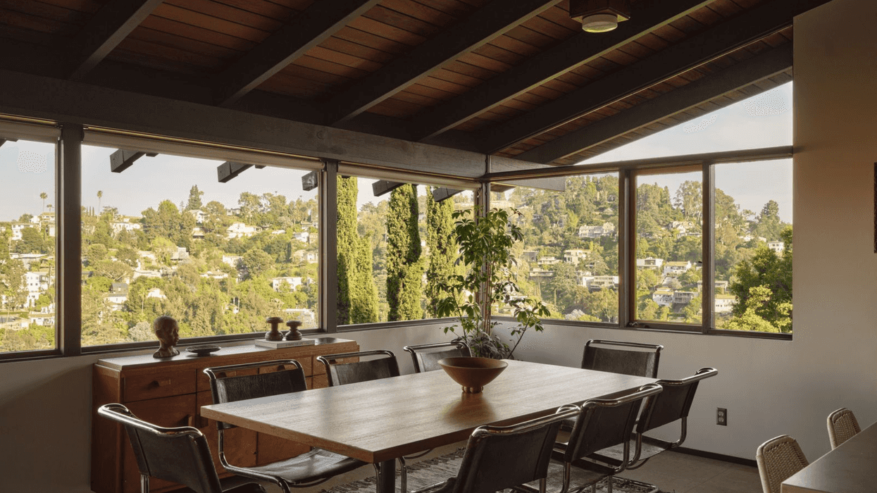 Mid-century dining room with large windows and a view of a hillside neighborhood.