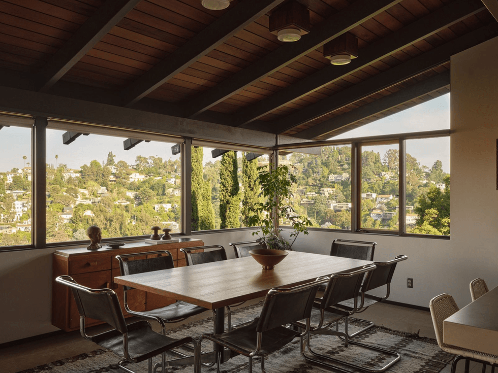Mid-century dining room with large windows and a view of a hillside neighborhood.