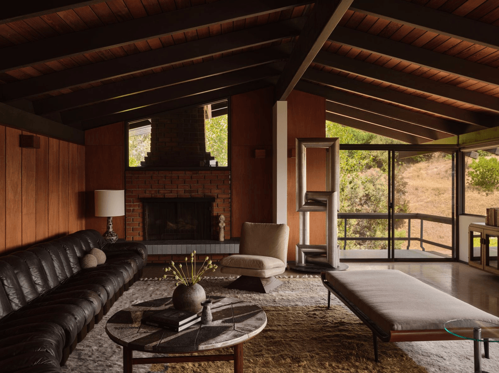 Mid-century modern living room with a fireplace, leather sofa, and large windows.