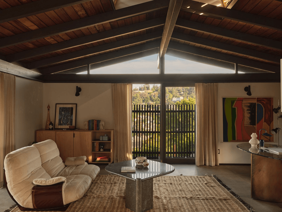 Mid-century modern living room with beige sofa, colorful art, and large window with garden view.
