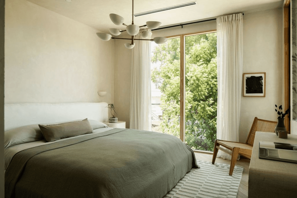 Minimalist bedroom with large window, green bedding, and wooden chair.