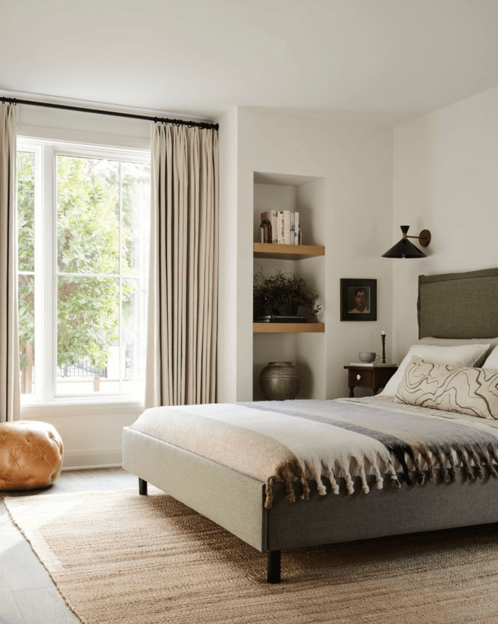 Minimalist bedroom with large window, soft rug, and earthy tones.