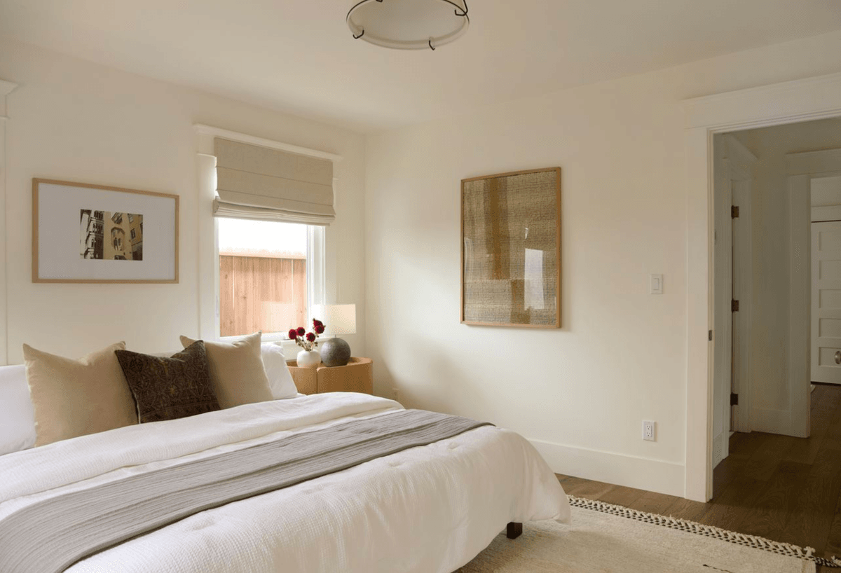 Minimalist bedroom with white bedding, neutral decor, and soft lighting.