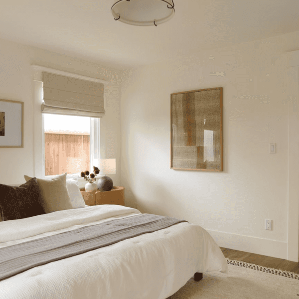 Minimalist bedroom with white bedding, neutral decor, and soft lighting.