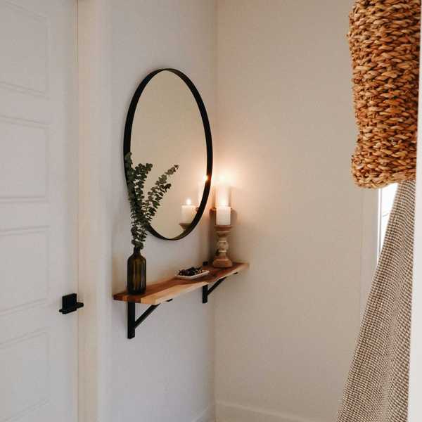 Minimalist entryway with round mirror, shelf, vase, and candle.