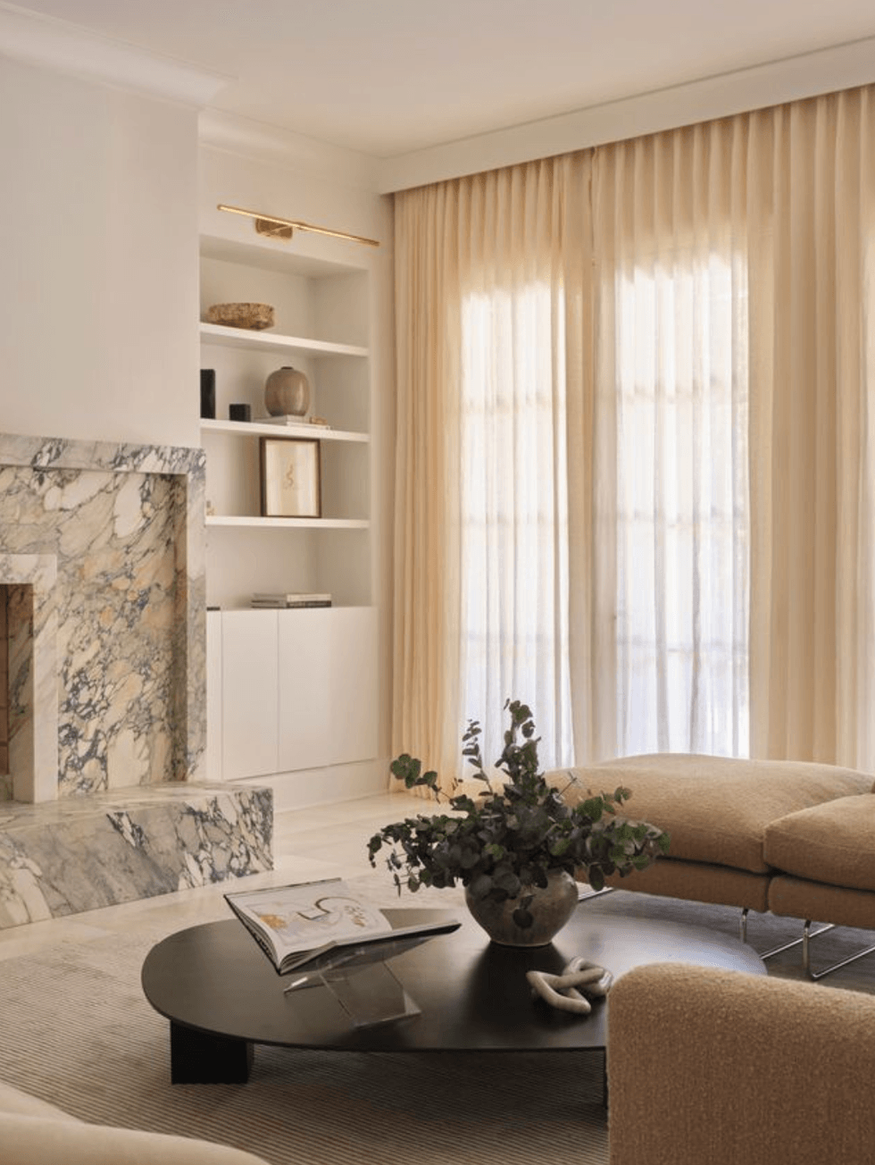 Minimalist living room with a marble fireplace, beige sofa, and coffee table with a plant.