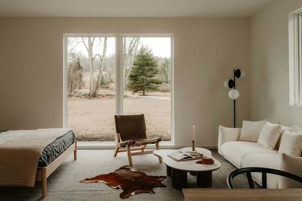 Minimalist room with large window, sofa, chair, and table, overlooking a grassy landscape.