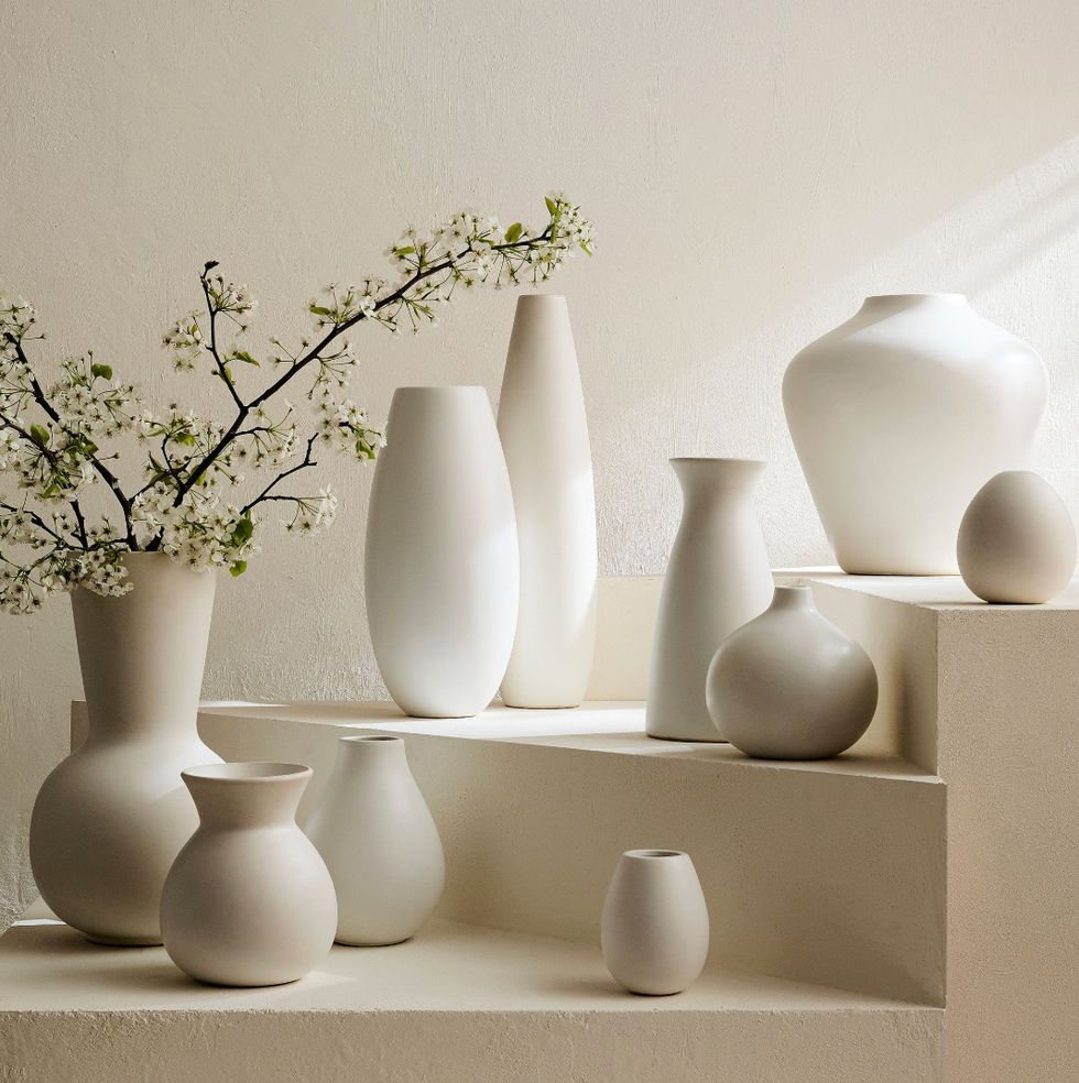 Minimalist white vases on steps; some with delicate flowering branches.