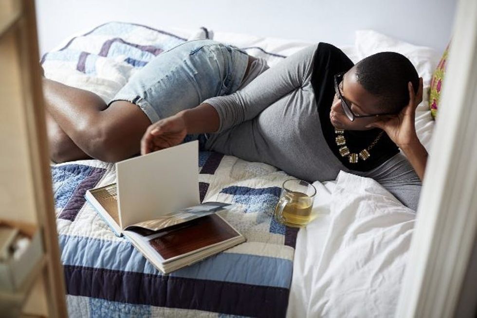 Mixed race woman drinking tea and reading on bed