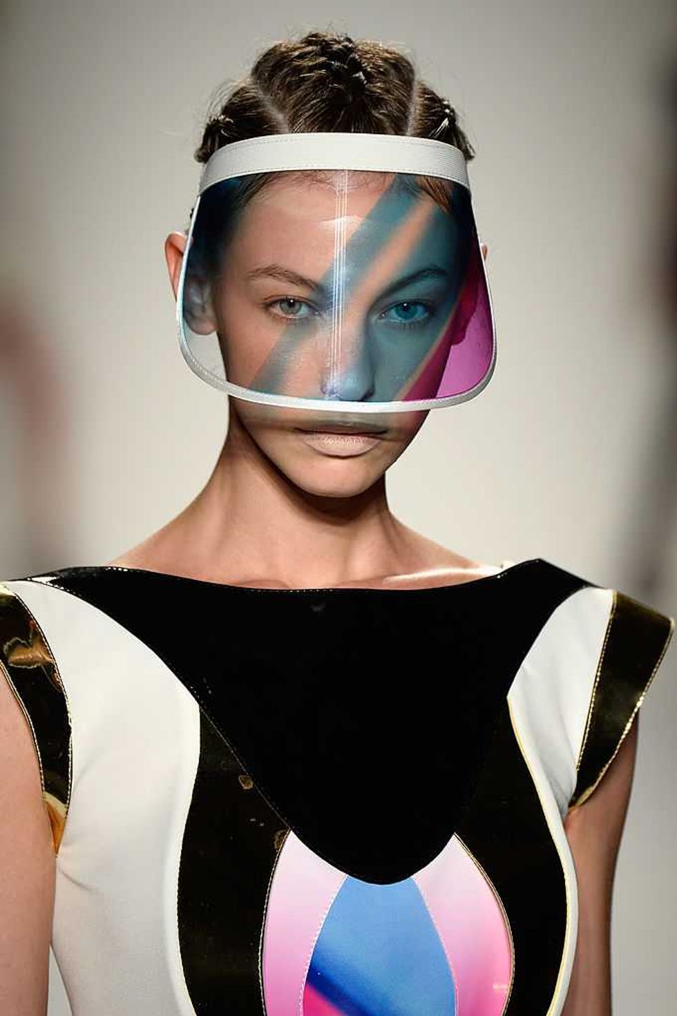 Model in futuristic visor and geometric-patterned outfit on runway.
