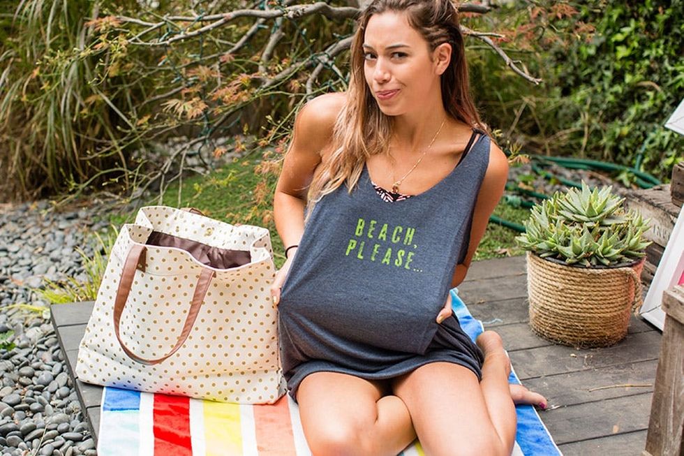 model wears gray Beach_Cover_Ups with green writing while sitting on a rainbow beach towel