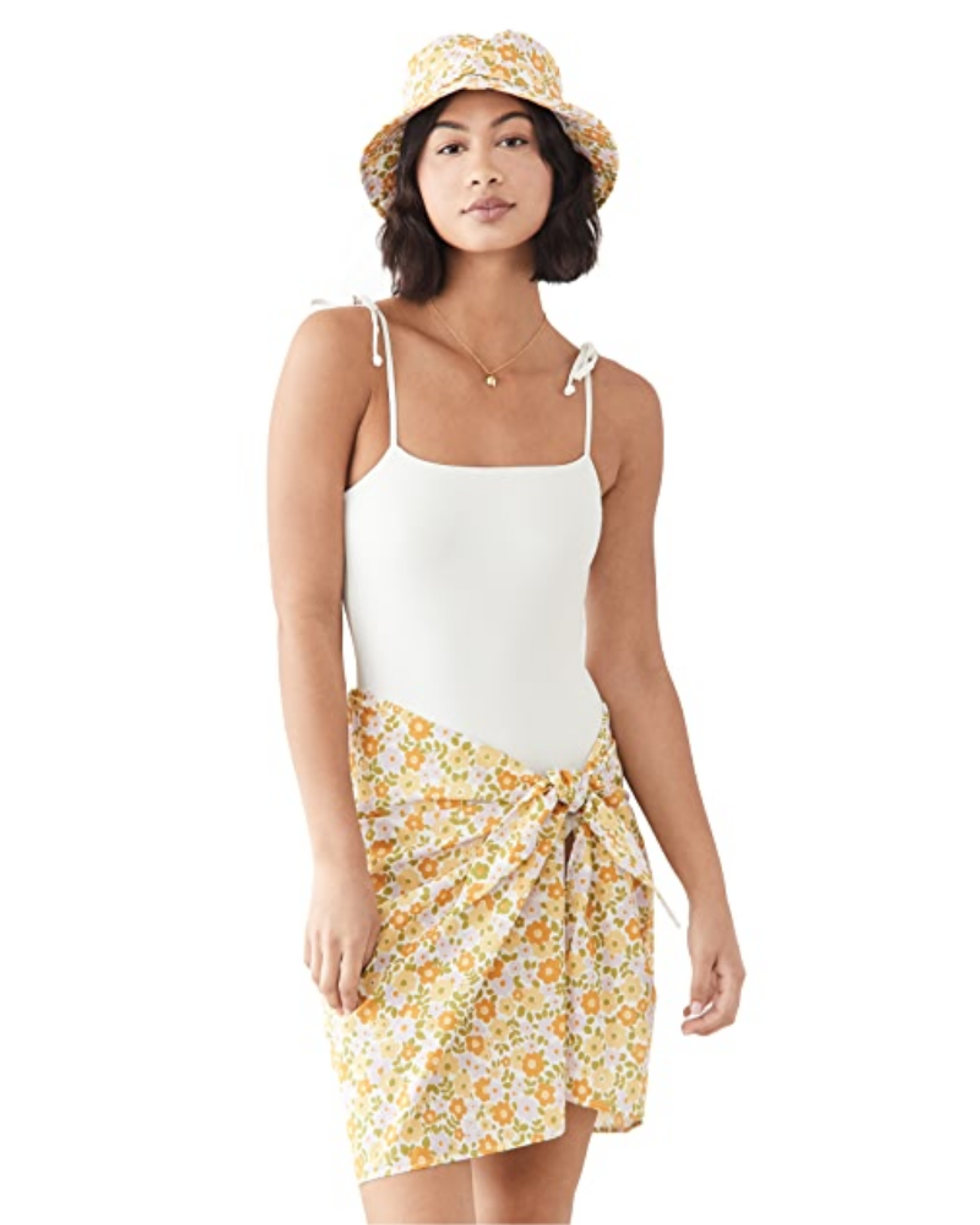 model wears orange, yellow, and green skirt set with a white bathing suit and bucket hat