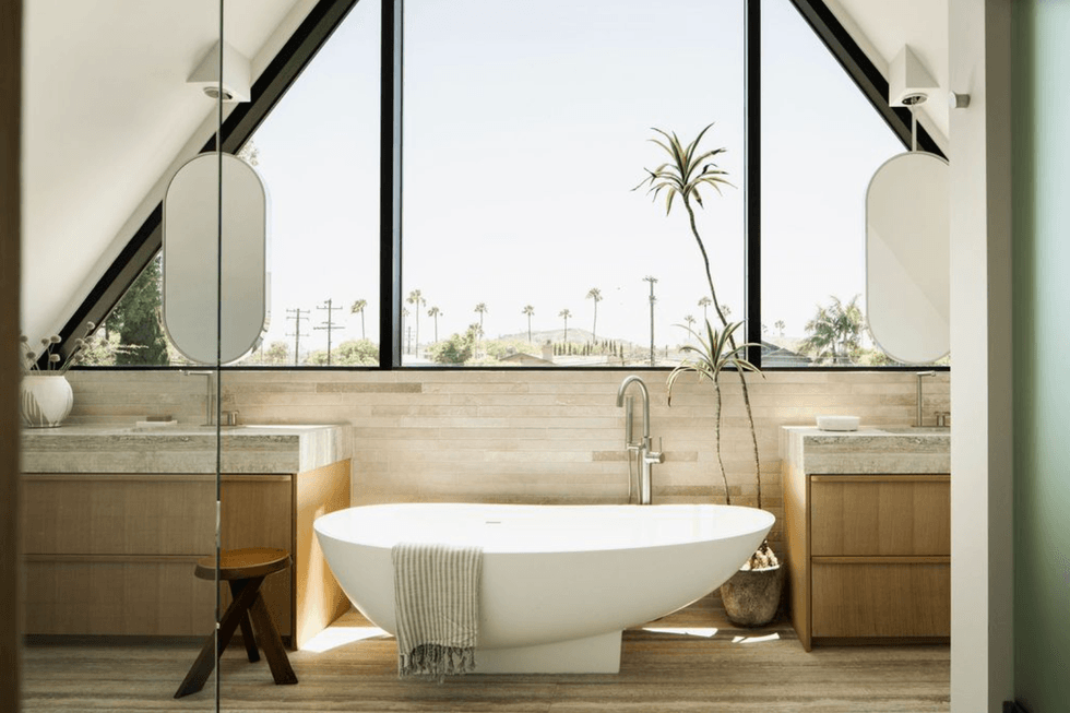 Modern bathroom with a freestanding tub beneath a large triangular window.