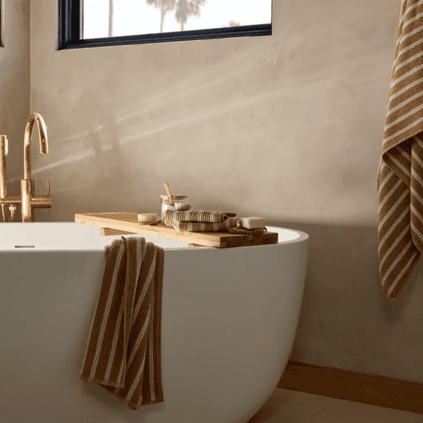 Modern bathroom with a white tub, wooden tray, and striped towels.