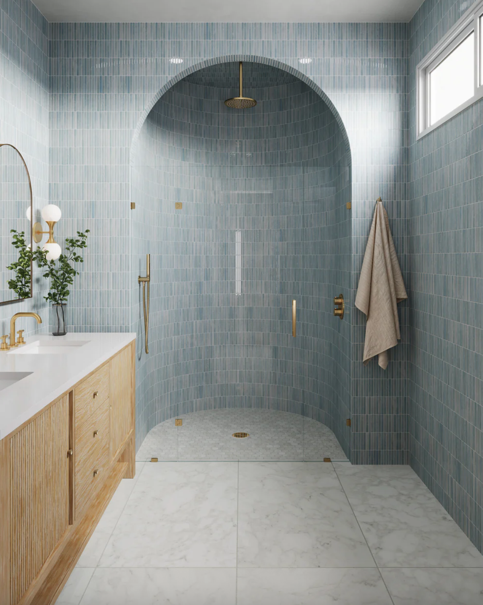 Modern bathroom with blue-tiled arched shower, wooden vanity, and marble floor.