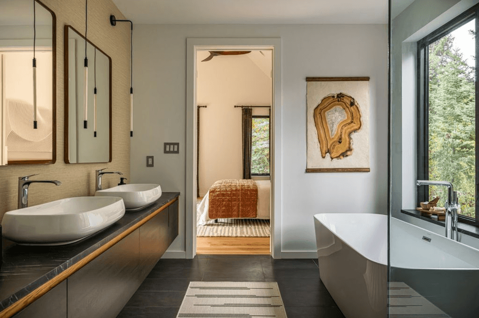 Modern bathroom with double sinks, free-standing tub, and view into a cozy bedroom.