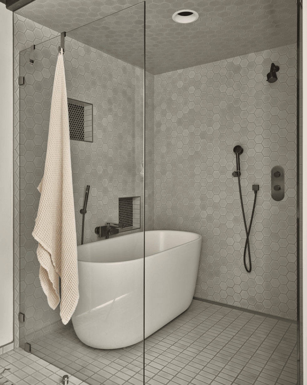 Modern bathroom with freestanding tub, glass enclosure, and hexagonal tile design.