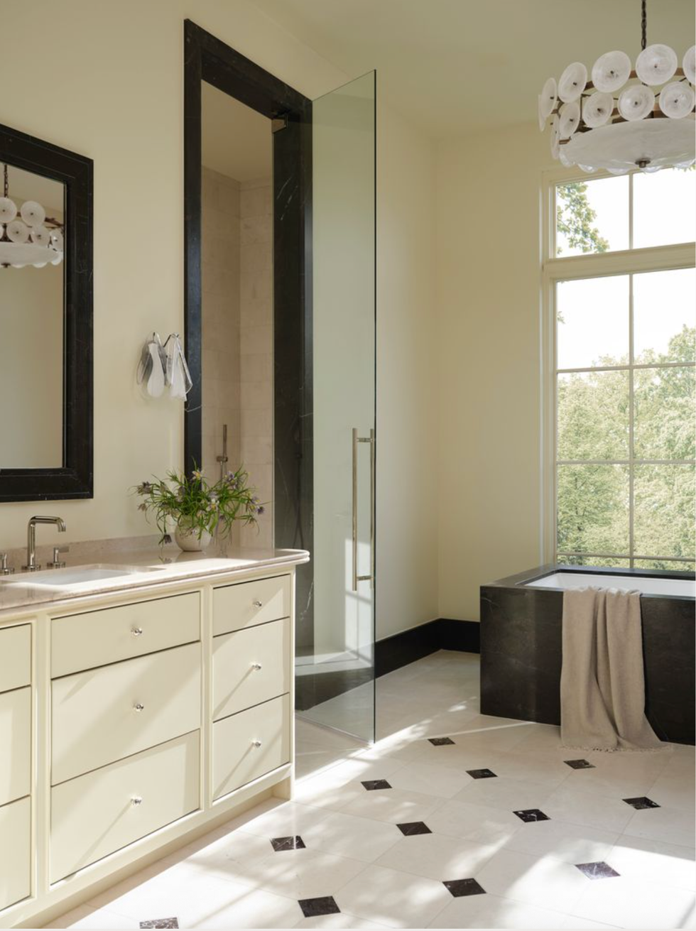 Modern bathroom with glass shower, tub, vanity, and large window with garden view.