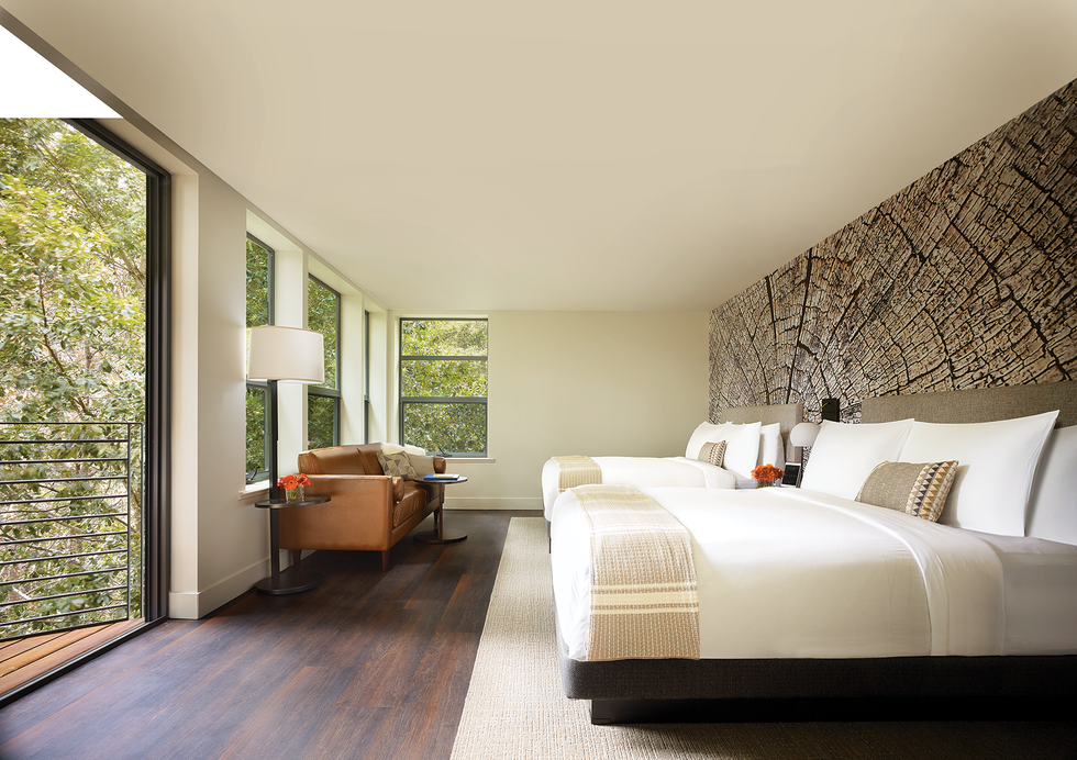 Modern bedroom with two beds, a patterned headboard, and large windows overlooking trees.