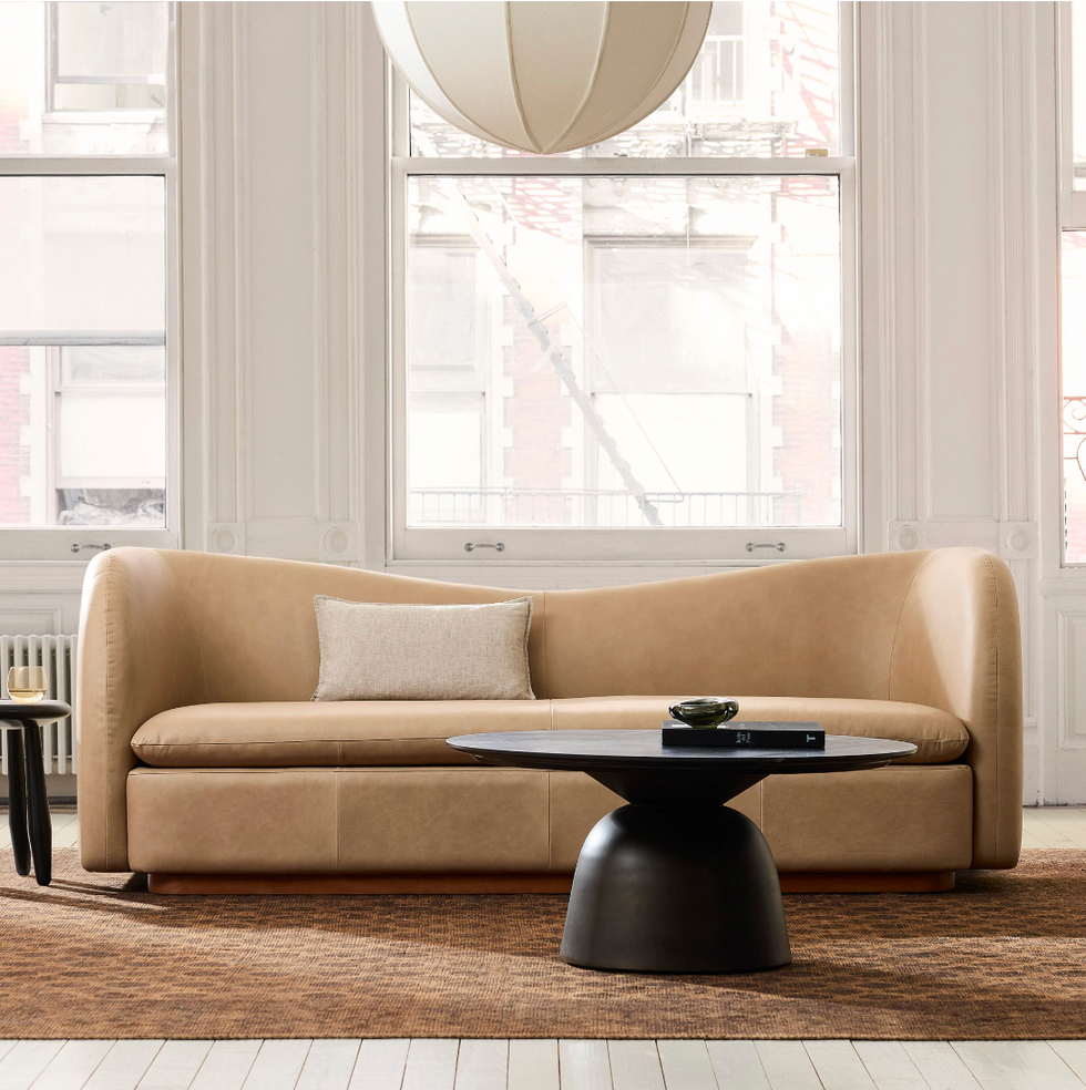 Modern beige sofa with pillow, black coffee table, large windows, and a round pendant light.